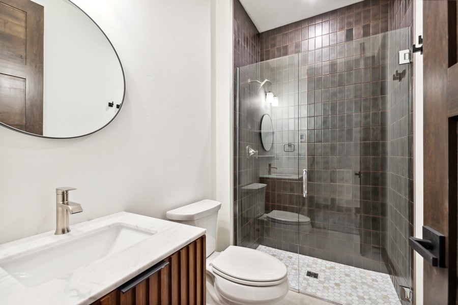 Bathroom with a marble vanity and glass shower lined with dark tile.