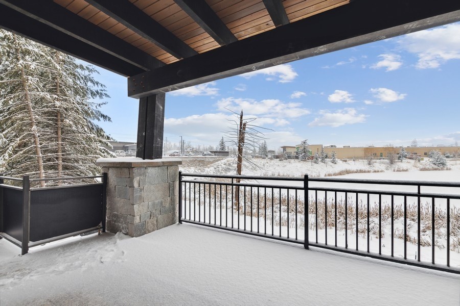 Covered patio with snow-covered floor and wetlands beyond a black metal railing.