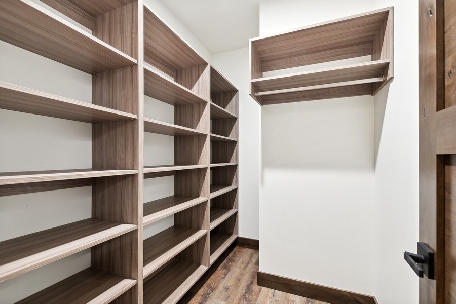 Walk-in closet with extensive walnut-toned built-in shelving and dark wood flooring.