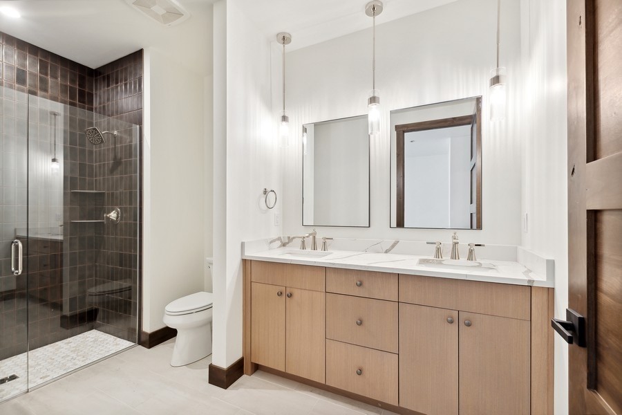 Modern bathroom with a double vanity and glass-enclosed dark-tile shower.