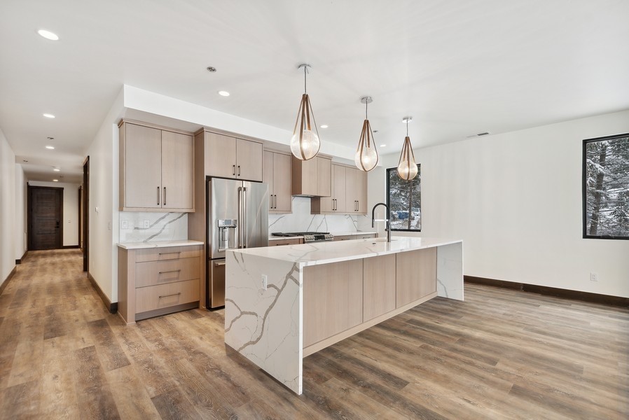 Modern kitchen with a large waterfall island, light wood cabinets, and pendant lights.