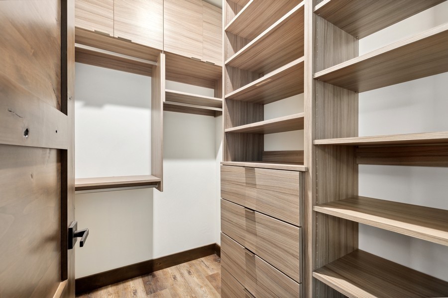 Walk-in closet with custom light wood shelving, drawers, and hanging space.