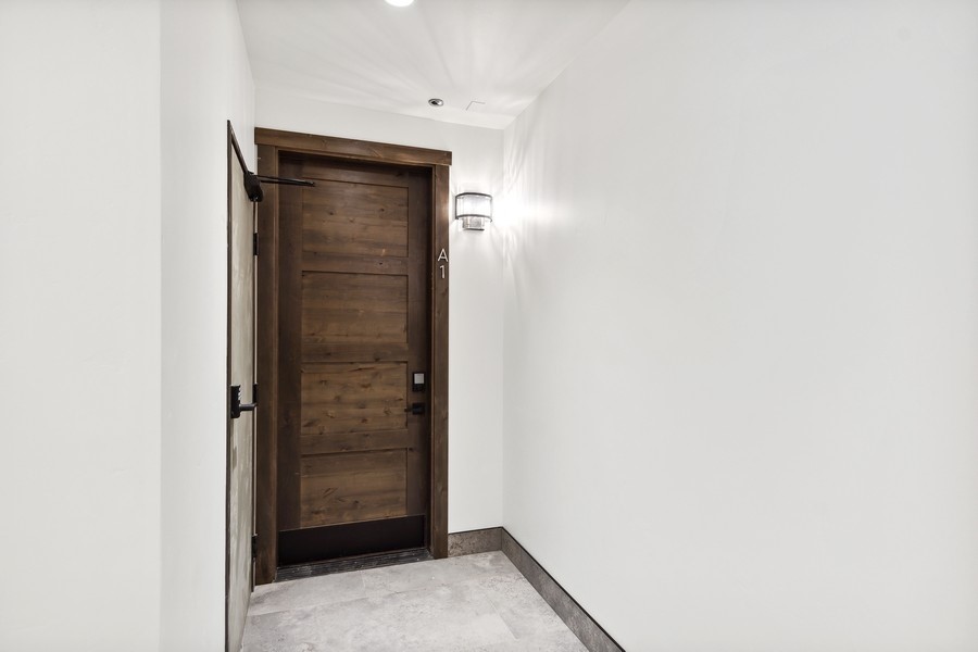 Entryway with a dark wood door, gray tile floor, and wall sconce.