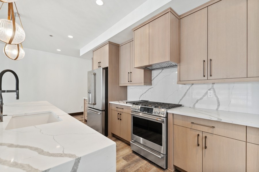 Modern kitchen with light wood cabinets, veined stone counters, a large island, and stainless steel appliances.