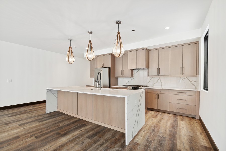 Kitchen with a large marble-look island, pale wood cabinets, and three pendant lights.