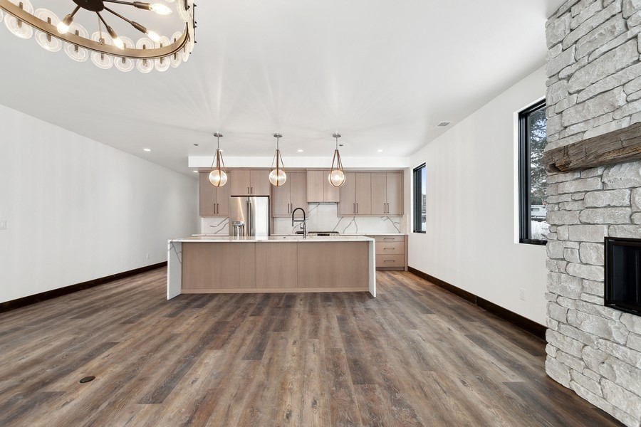 Unfurnished kitchen with a large island, light wood cabinets, and a stone fireplace.