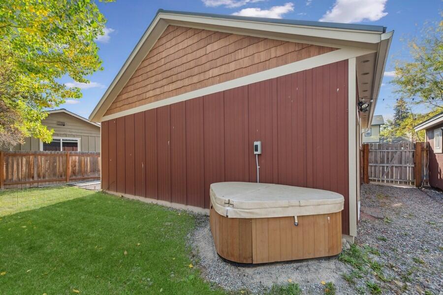 Backyard with a covered hot tub beside a red-sided detached garage and fenced lawn.