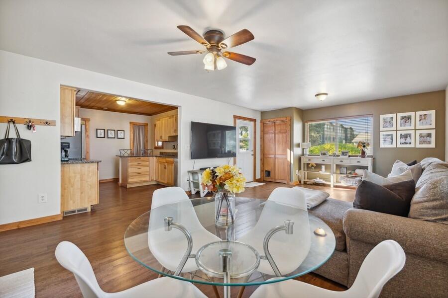 Living and dining area with hardwood floors, a glass table, sectional sofa, and adjoining wood-cabinet kitchen.