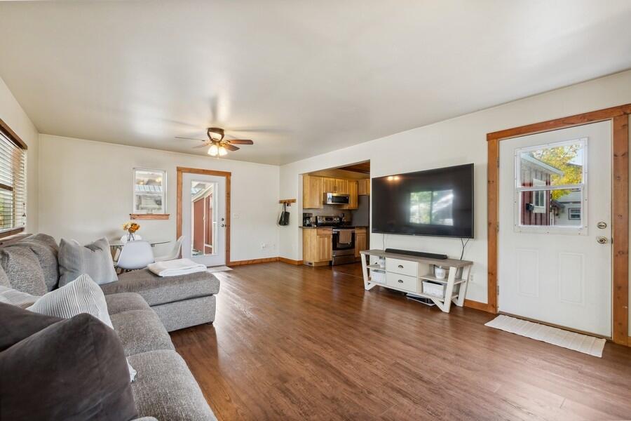 Living room with a gray sectional, television, wood-look floors, and an adjoining compact kitchen.