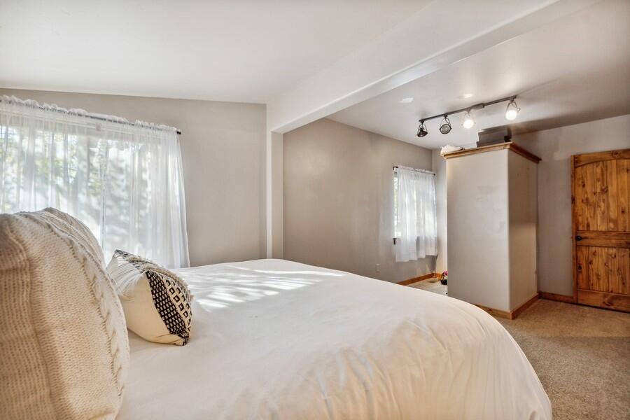 Bedroom with a large white bed, sheer-curtained windows, and a wooden closet door.