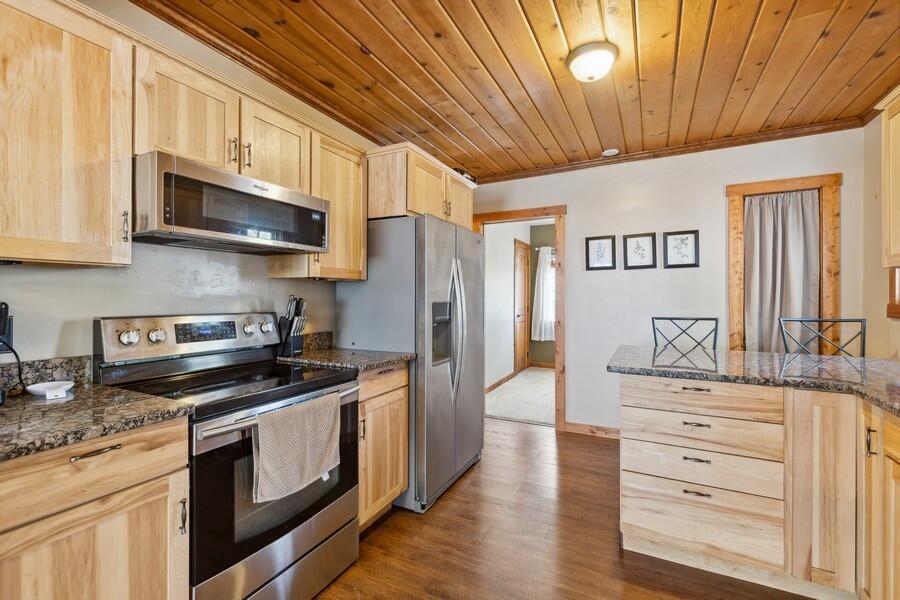 Kitchen with light wood cabinets, stainless steel appliances, granite counters, and a wood-paneled ceiling.