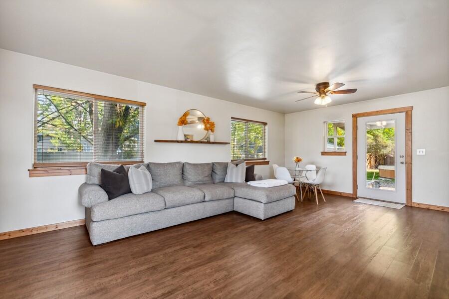 Living room with a gray sectional sofa, warm wood floors, and a dining nook beside a glass door.