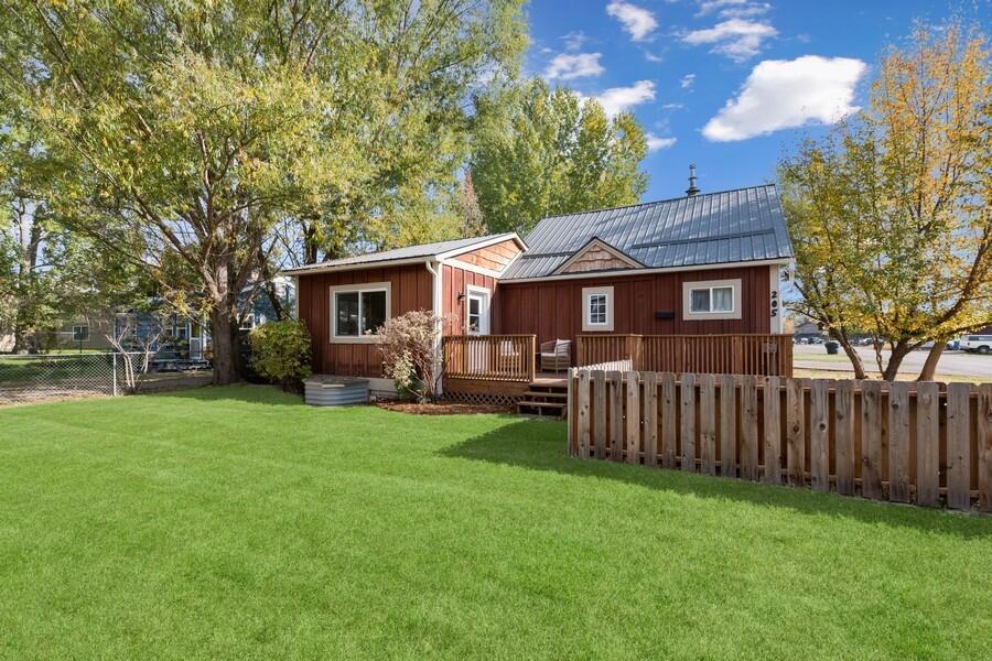 Red-brown home with a metal roof and porch behind a fenced green lawn.