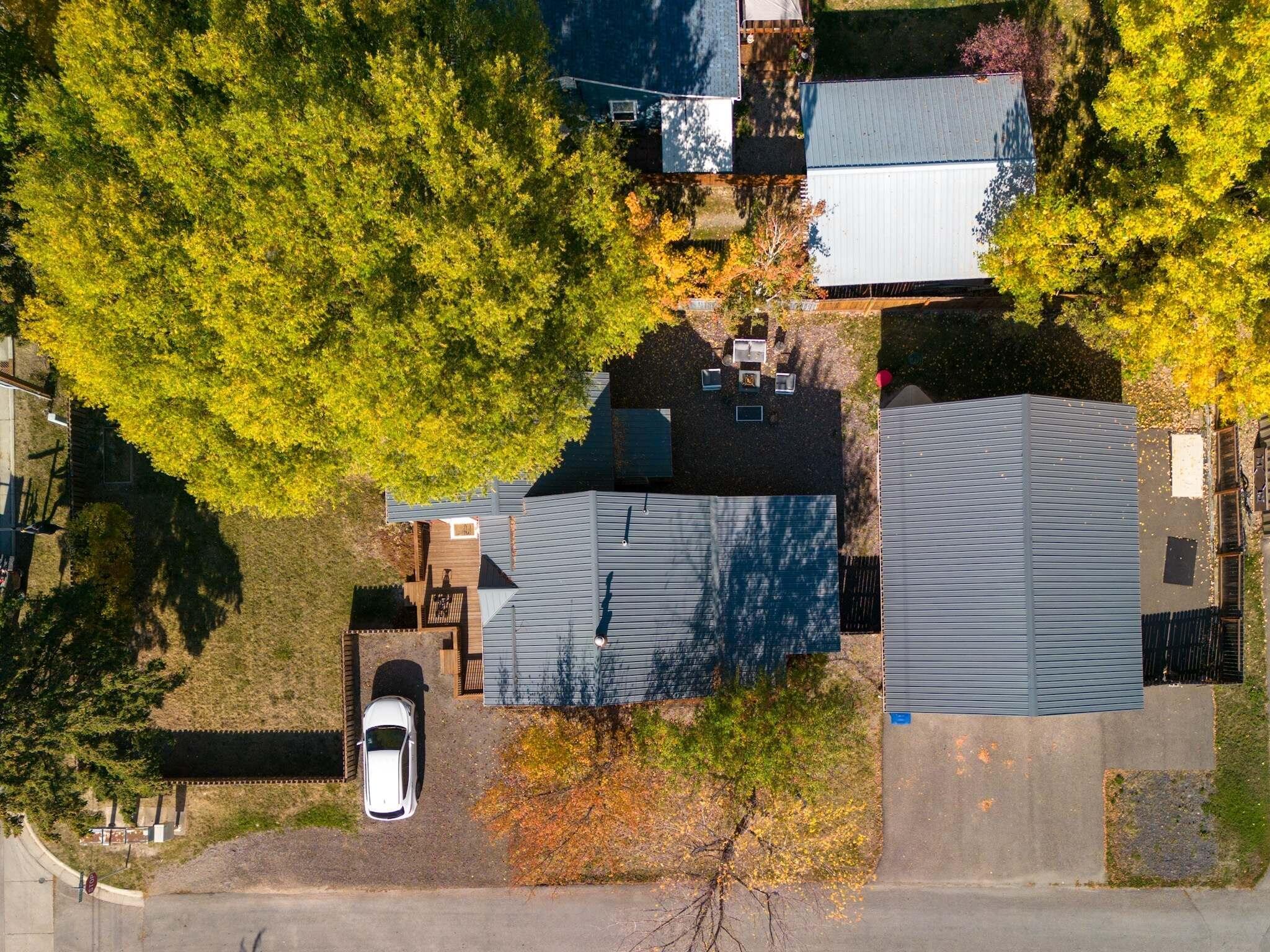 Aerial view of gray-roofed buildings and parking area among yellow autumn trees.