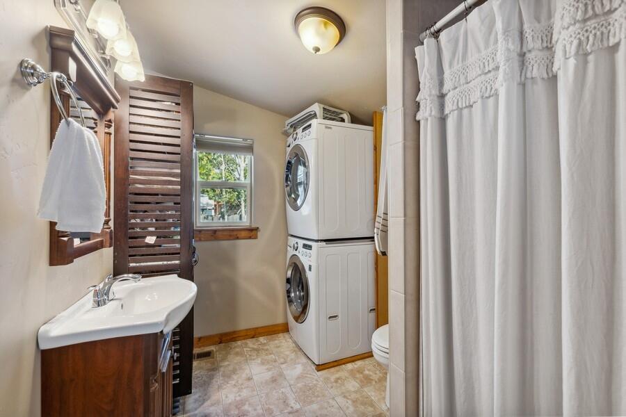 Bathroom and laundry area with a dark wood vanity, stacked washer and dryer, and shower curtain.