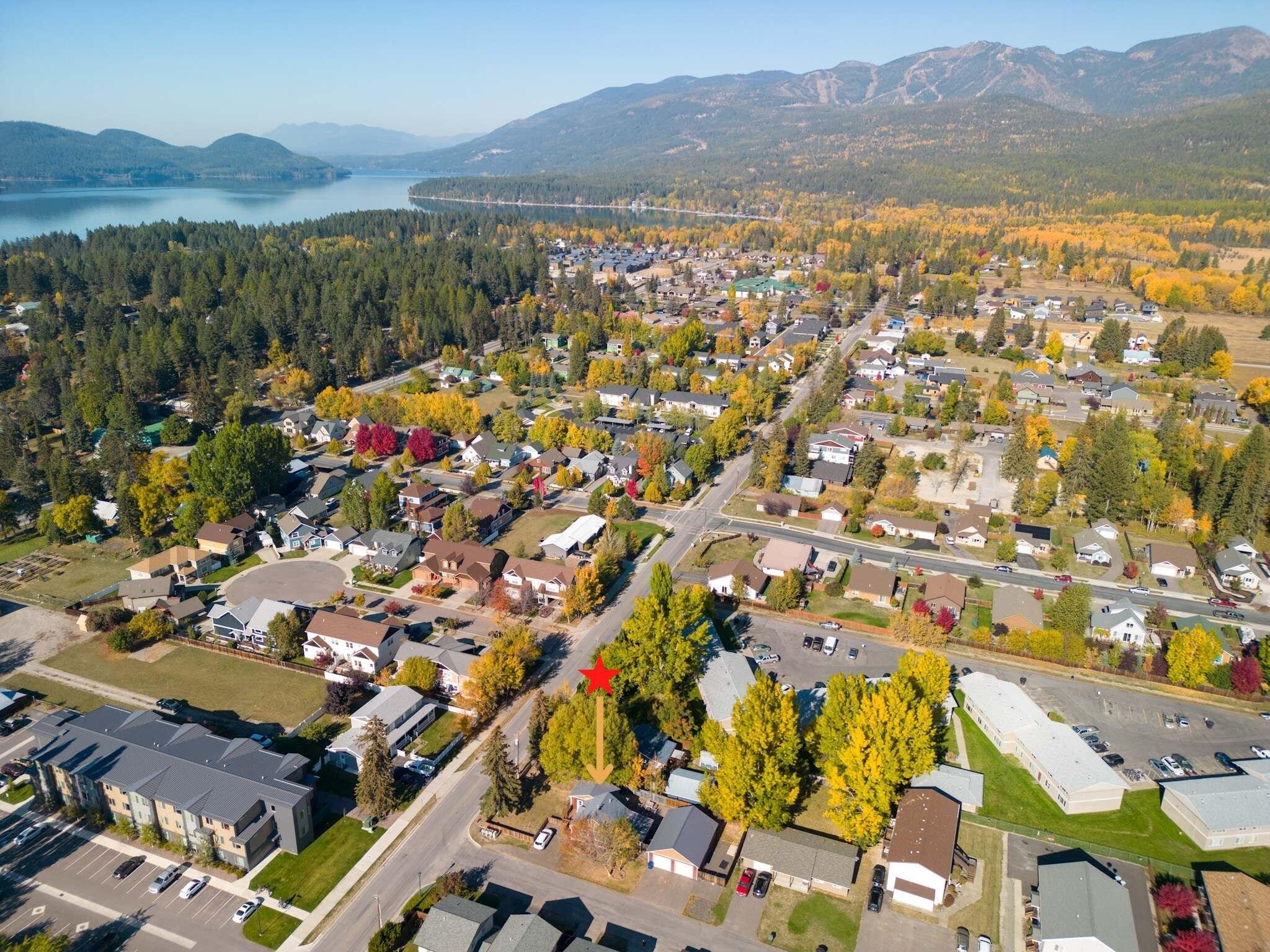 Aerial view of the marked property in an autumn neighborhood near a lake and mountains.