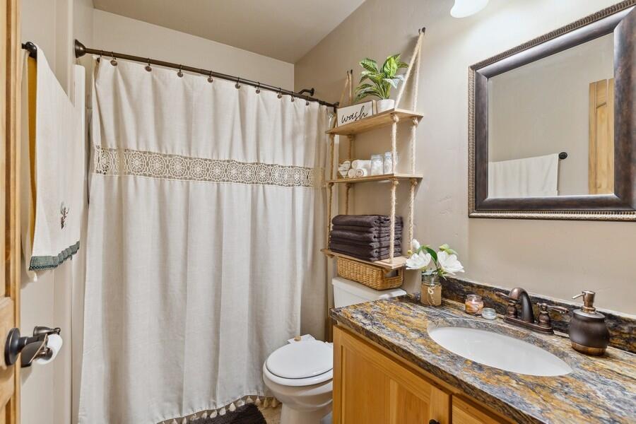 Bathroom with a wooden vanity, stone countertop, and white shower curtain.