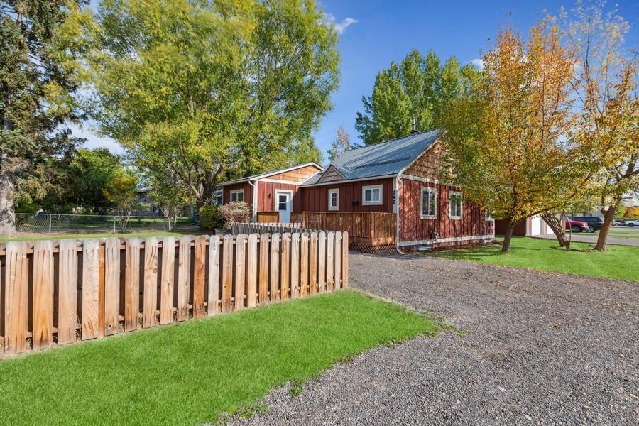 Red-sided home with rooftop solar panels, a wooden fence, and gravel driveway beneath autumn trees.