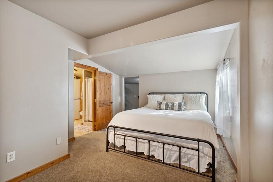 Bedroom with a black metal bed and white bedding beside a wooden bathroom doorway.