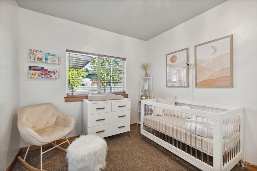 Bright nursery with a white crib, matching dresser, cream chair, and neutral wall art.