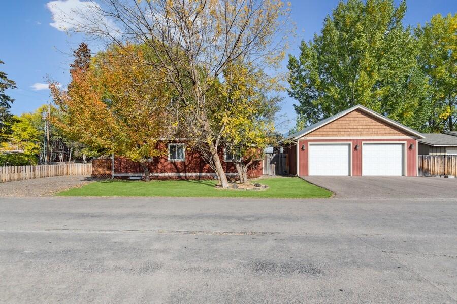 Red two-car garage beside a tree-shaded lawn, wooden fence, and paved driveway.