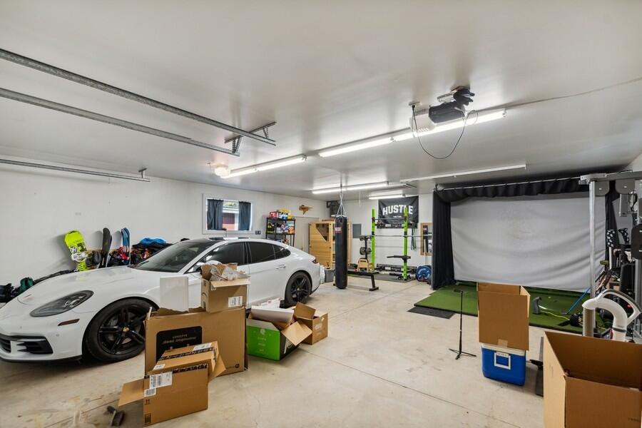 Garage with a white sports car, workout equipment, and a large projection screen.