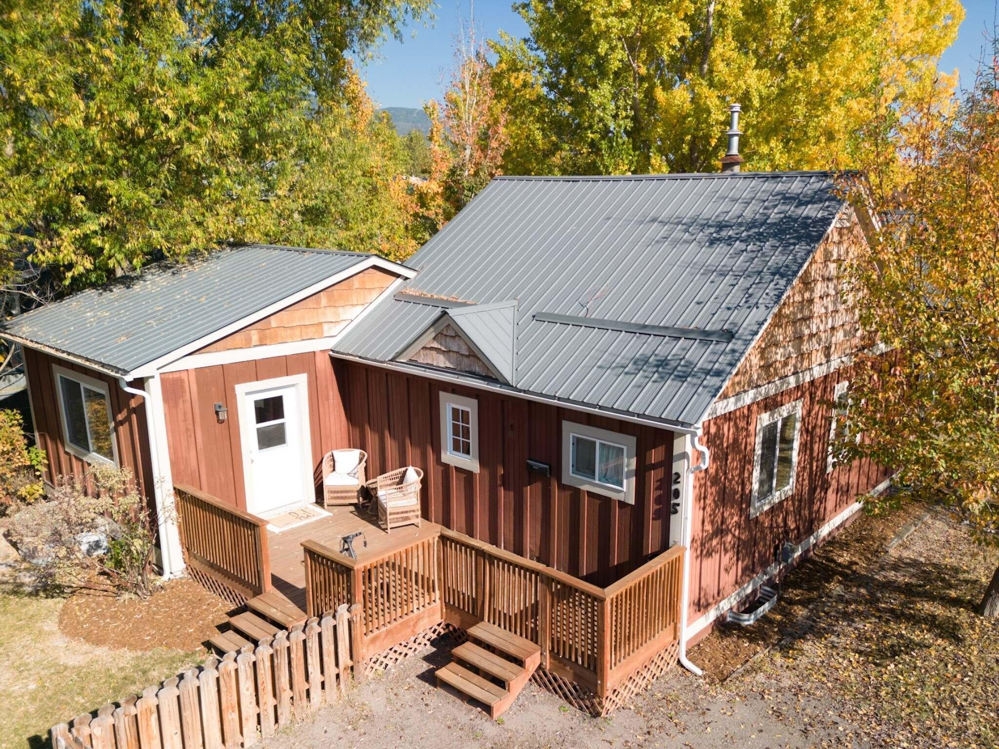 Red-brown home with gray metal roofs and a wooden deck among autumn trees.