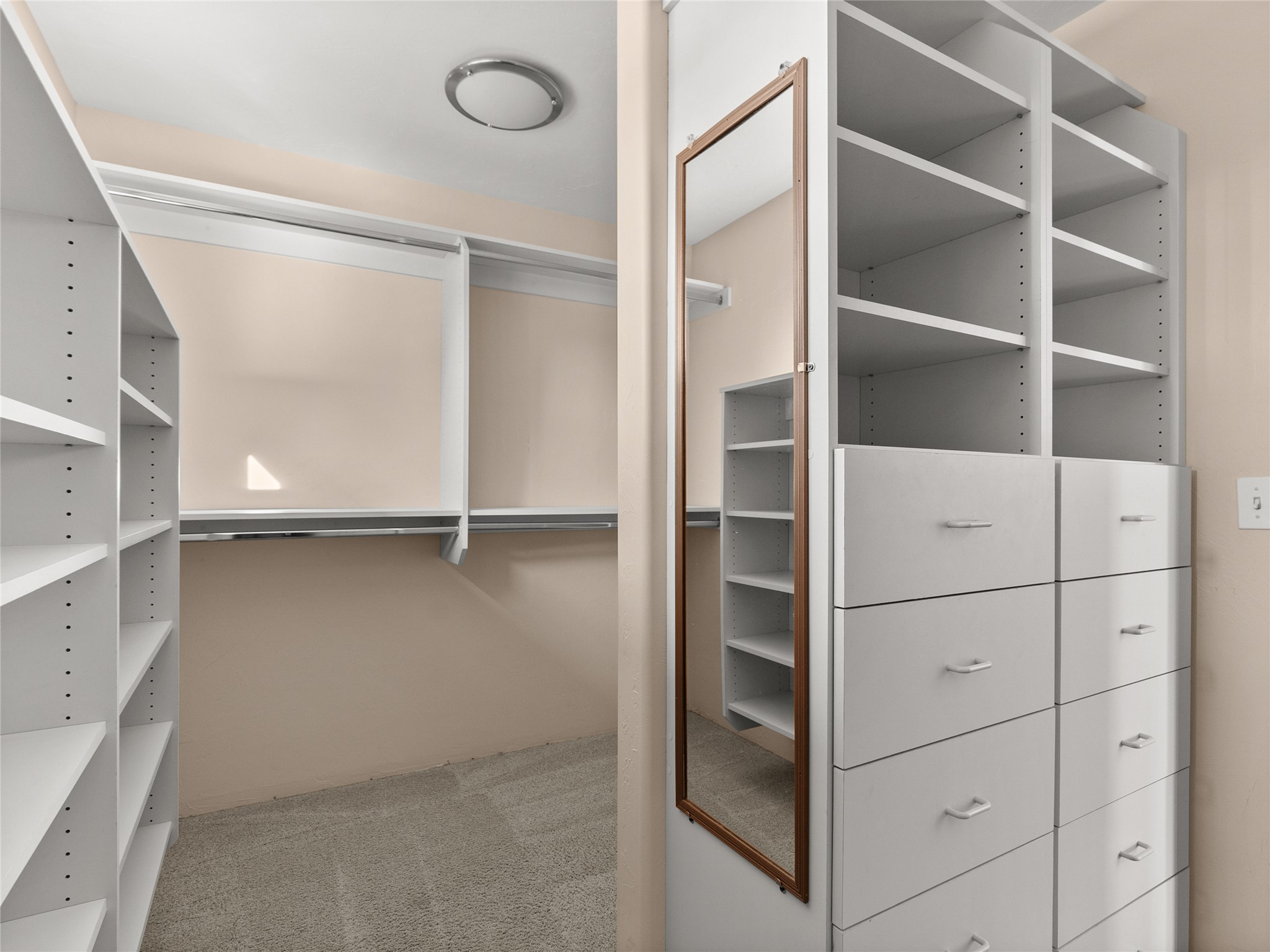 Walk-in closet with built-in white shelves and drawers and a full-length mirror.