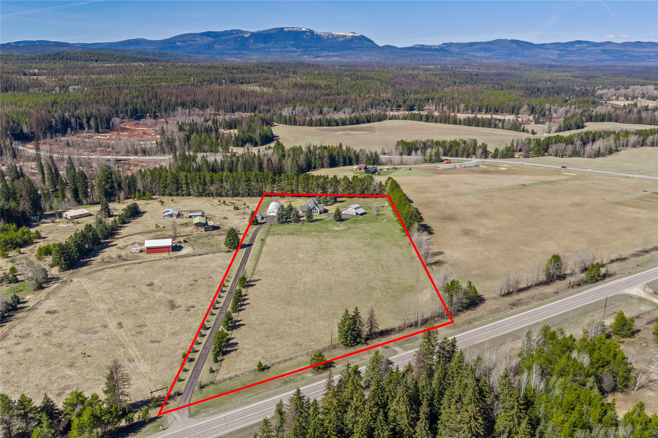Aerial view of a rural property outlined in red, with open acreage, several buildings, and mountains beyond.
