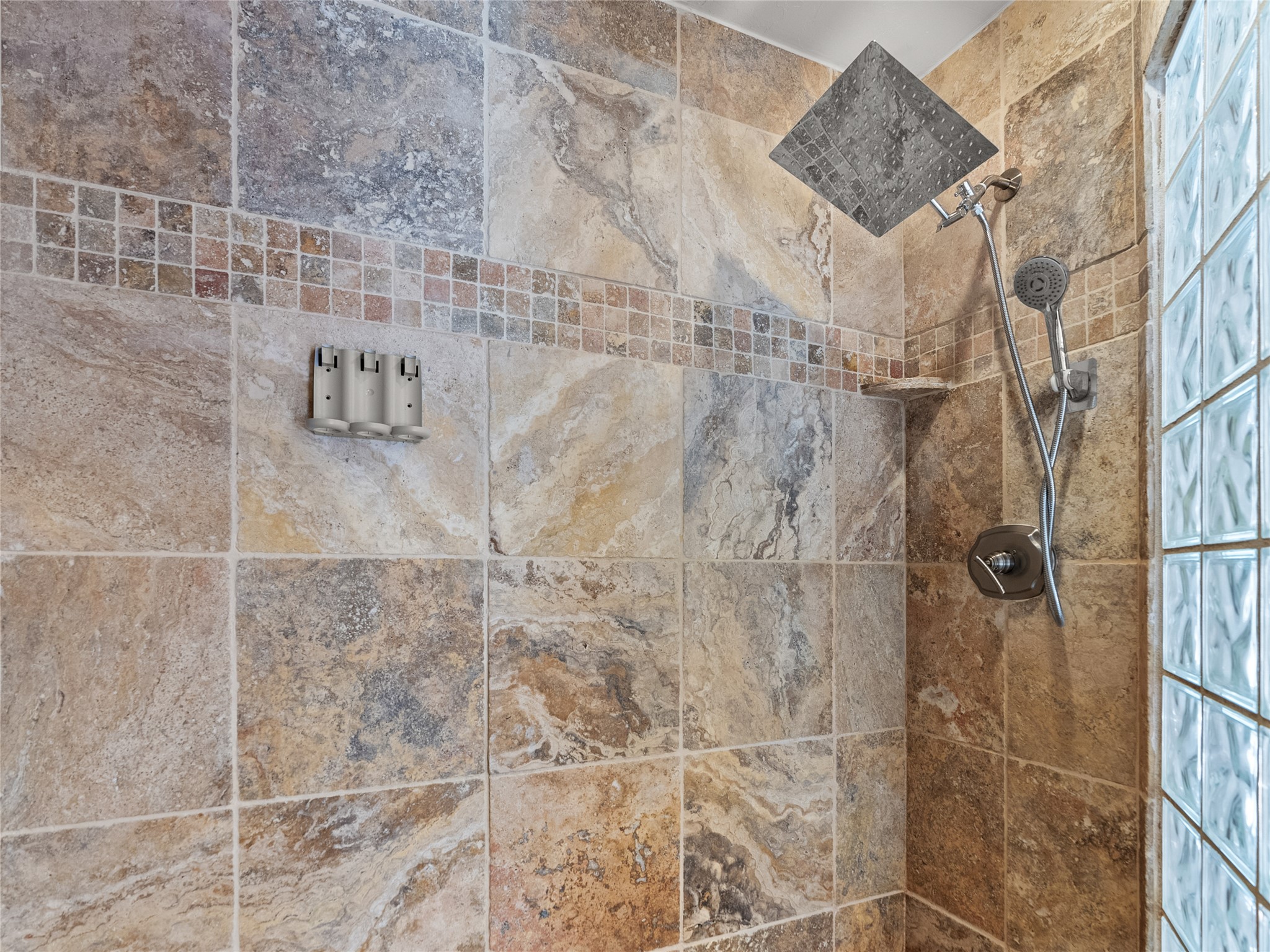 Stone-tiled shower with a square rain showerhead and glass-block wall.