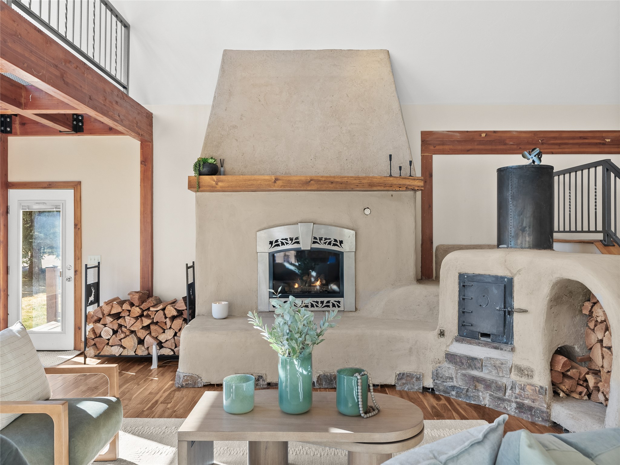 Living room with a large plaster fireplace, exposed timber beams, and stacked firewood.