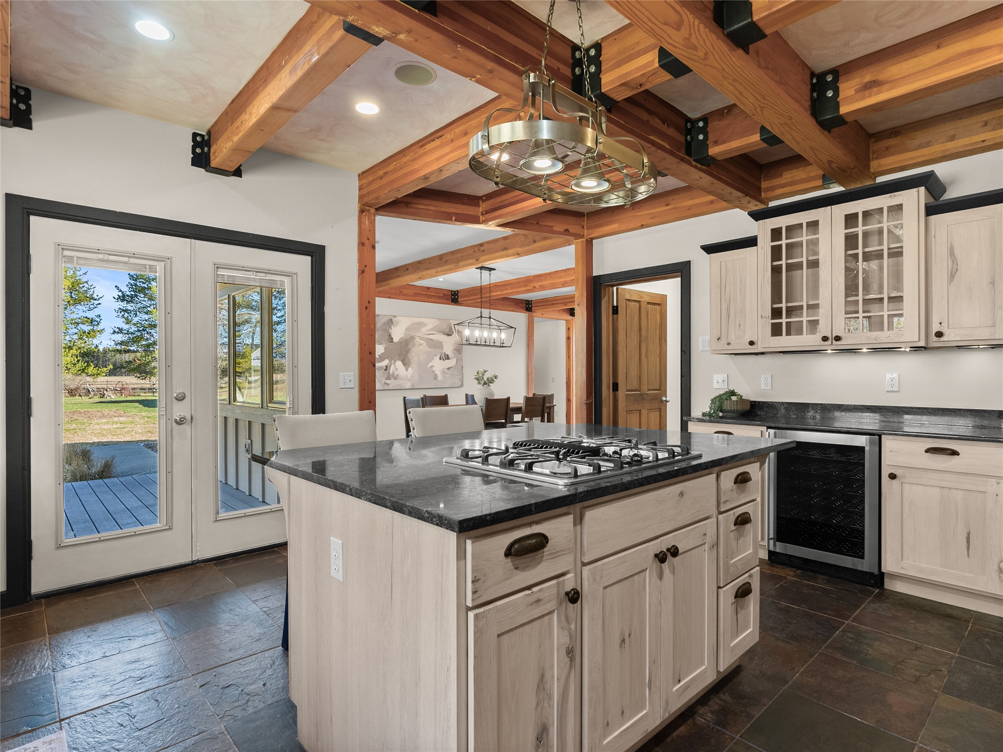 Kitchen with a black stone island, pale wood cabinetry, and exposed timber ceiling beams.