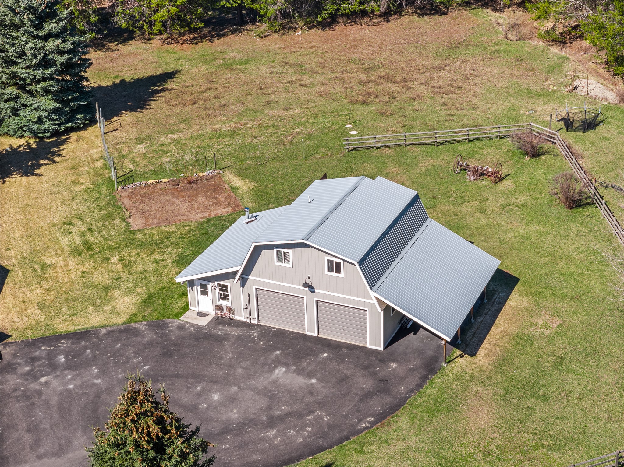 Aerial view of a gray workshop with two garage doors, a metal roof, and a fenced grassy yard.