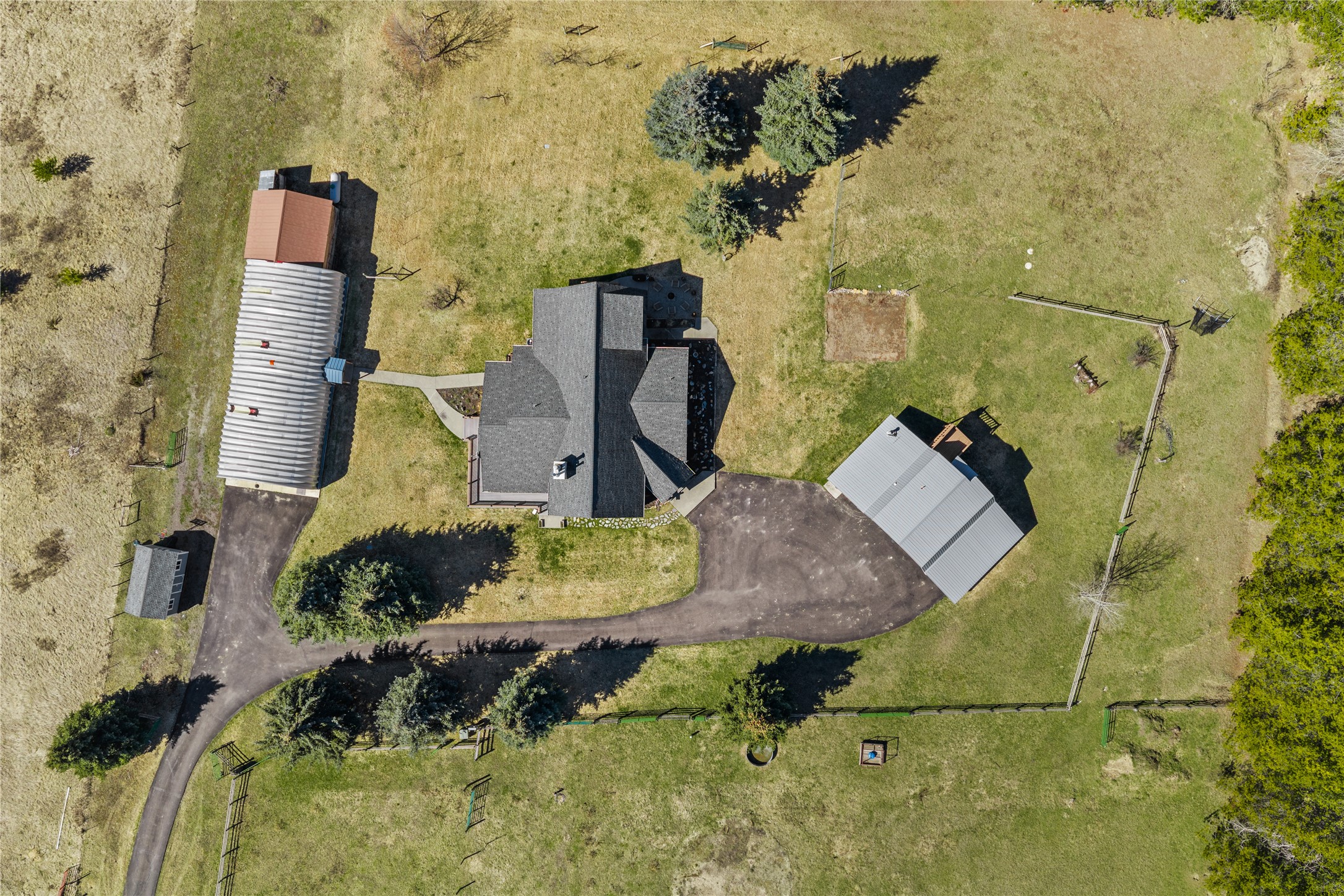 Aerial view of a house and outbuildings surrounded by fenced grounds and a curved driveway.