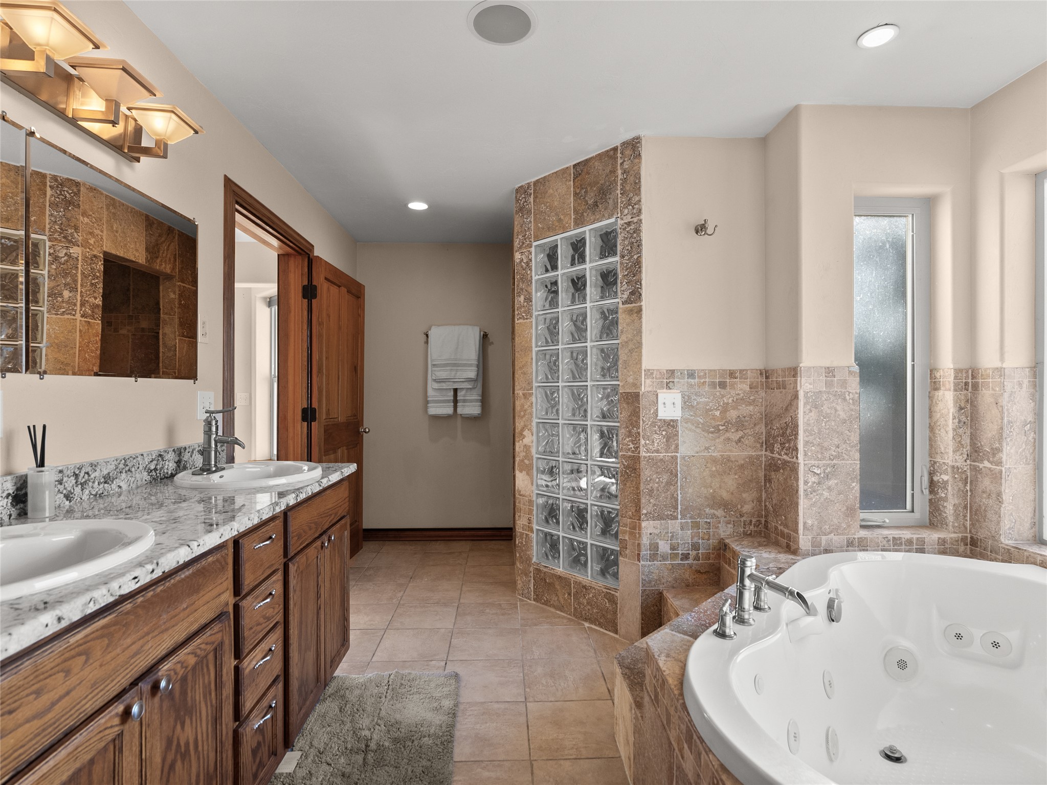 Bathroom with a jetted soaking tub, glass-block divider, and double-sink granite vanity.