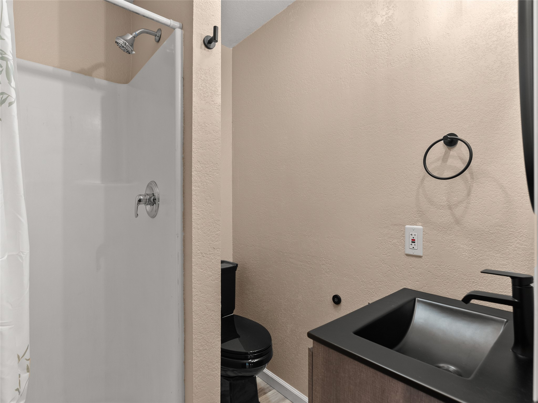 Bathroom with a white shower, black toilet, and dark vessel sink on a wood-toned vanity.