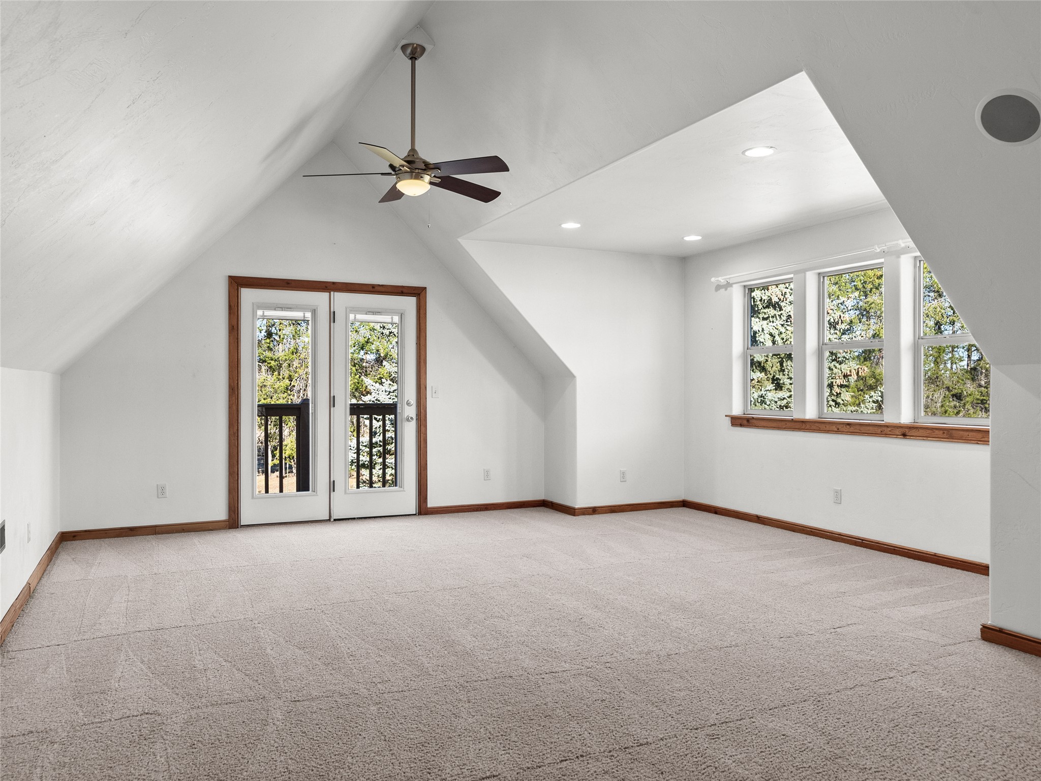 Empty carpeted room with a vaulted ceiling, ceiling fan, and glass doors to a balcony.