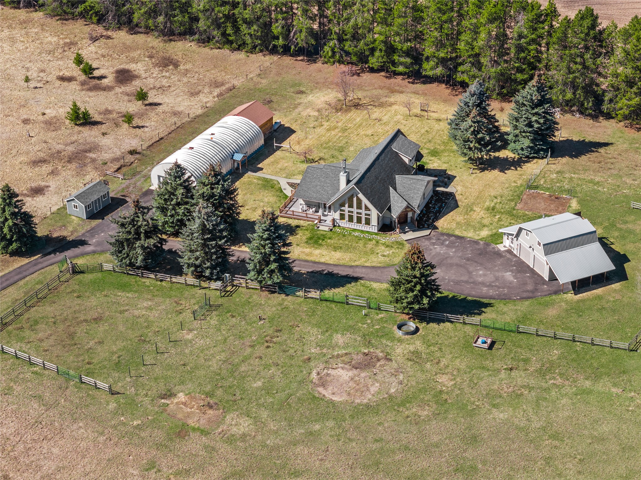 Aerial view of a rural home with a large outbuilding, detached barn, and fenced pasture.