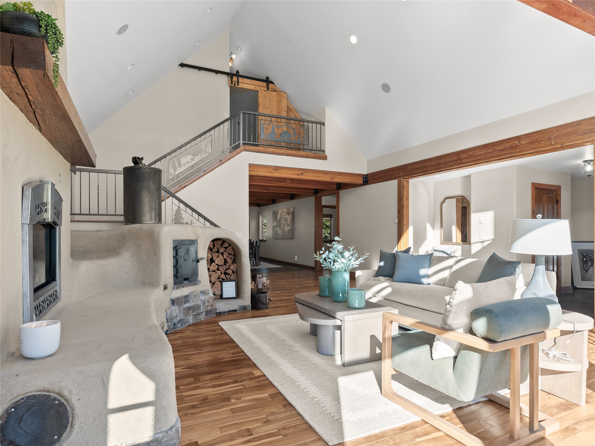 Vaulted living room with a large sculpted masonry fireplace, loft staircase, and cream seating.
