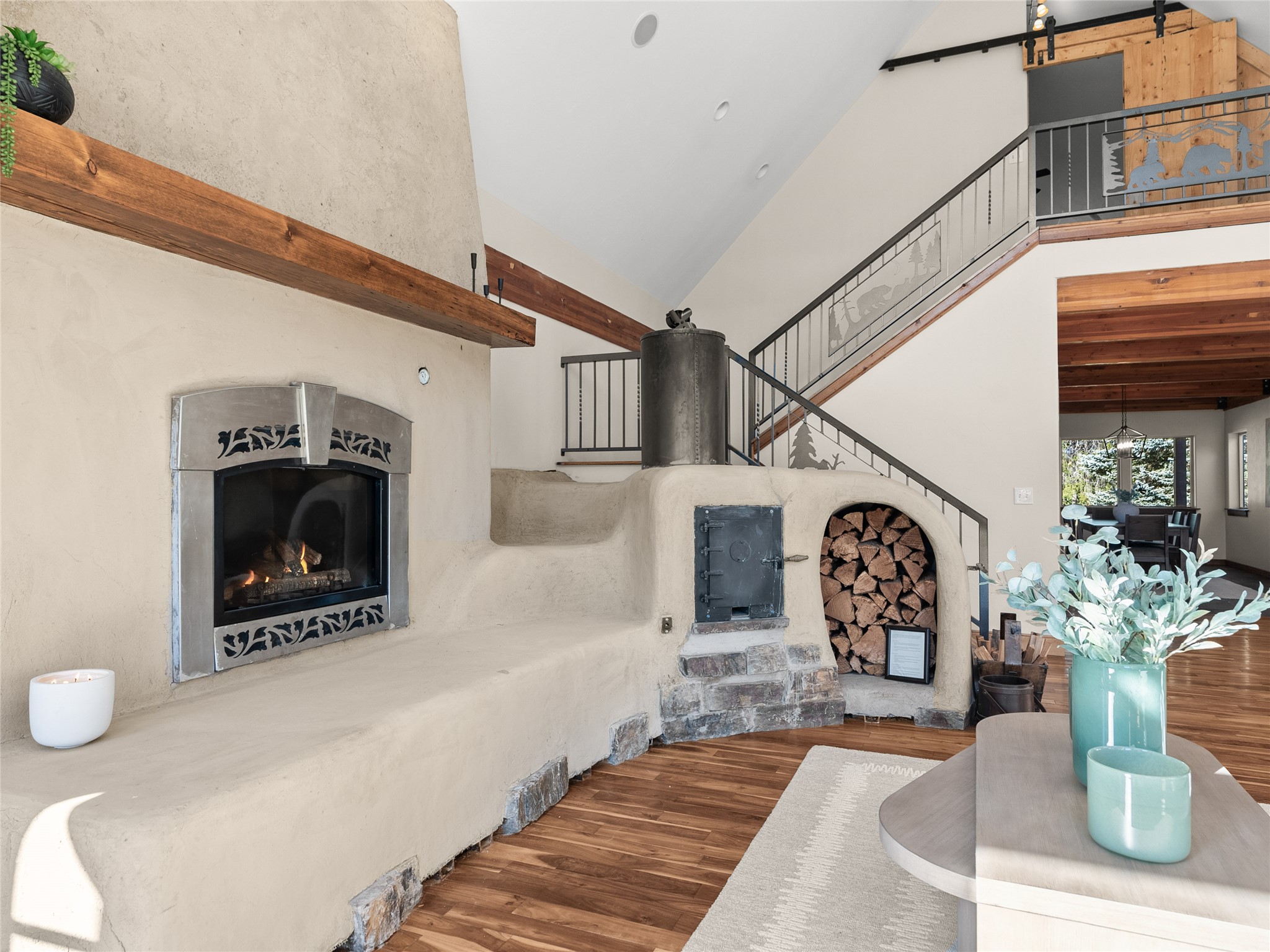 Living area with a sculpted adobe fireplace, arched wood-storage niche, and staircase with metal railings.