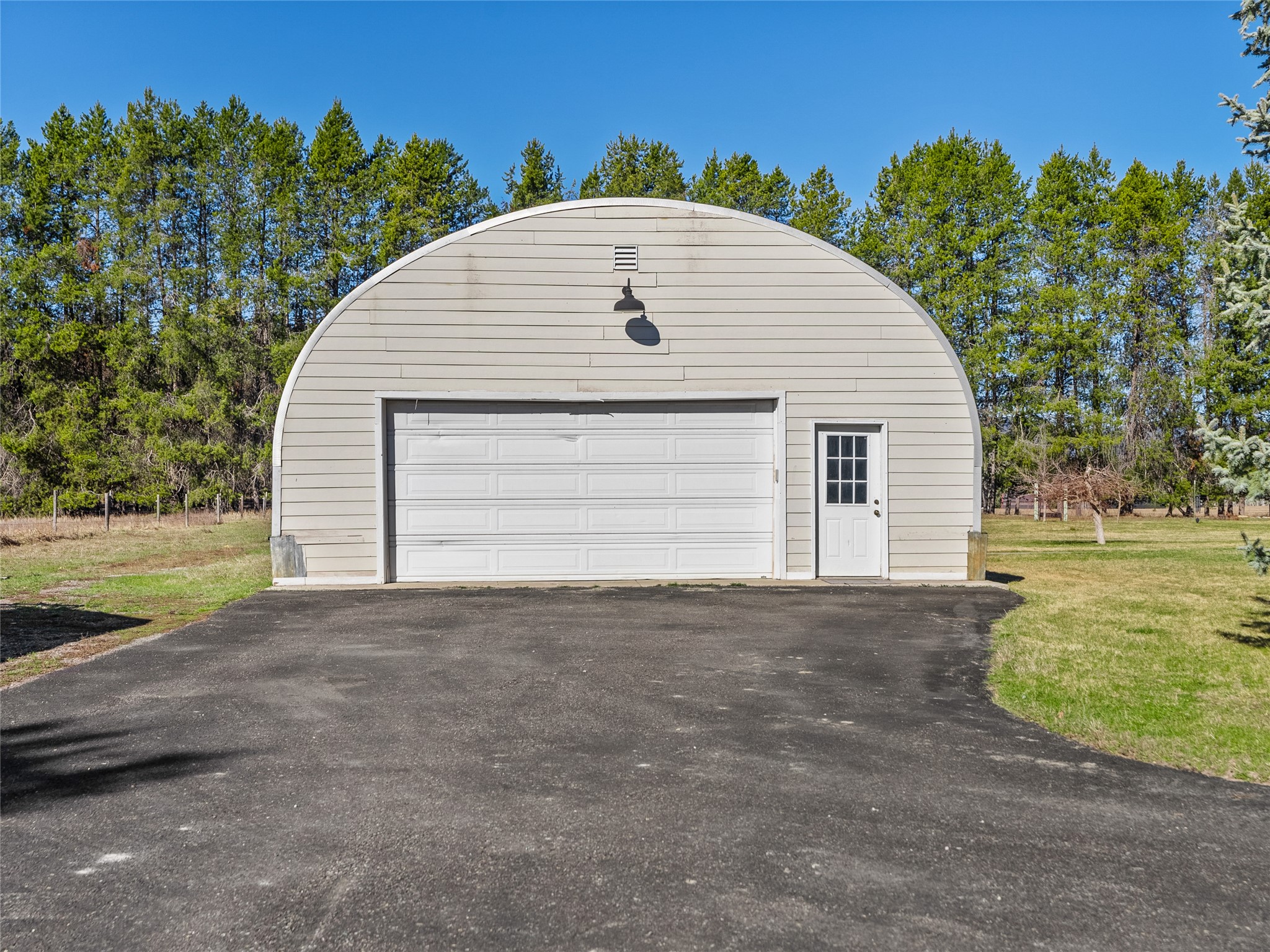 Detached arched-roof garage with a wide double door and paved driveway, backed by trees.