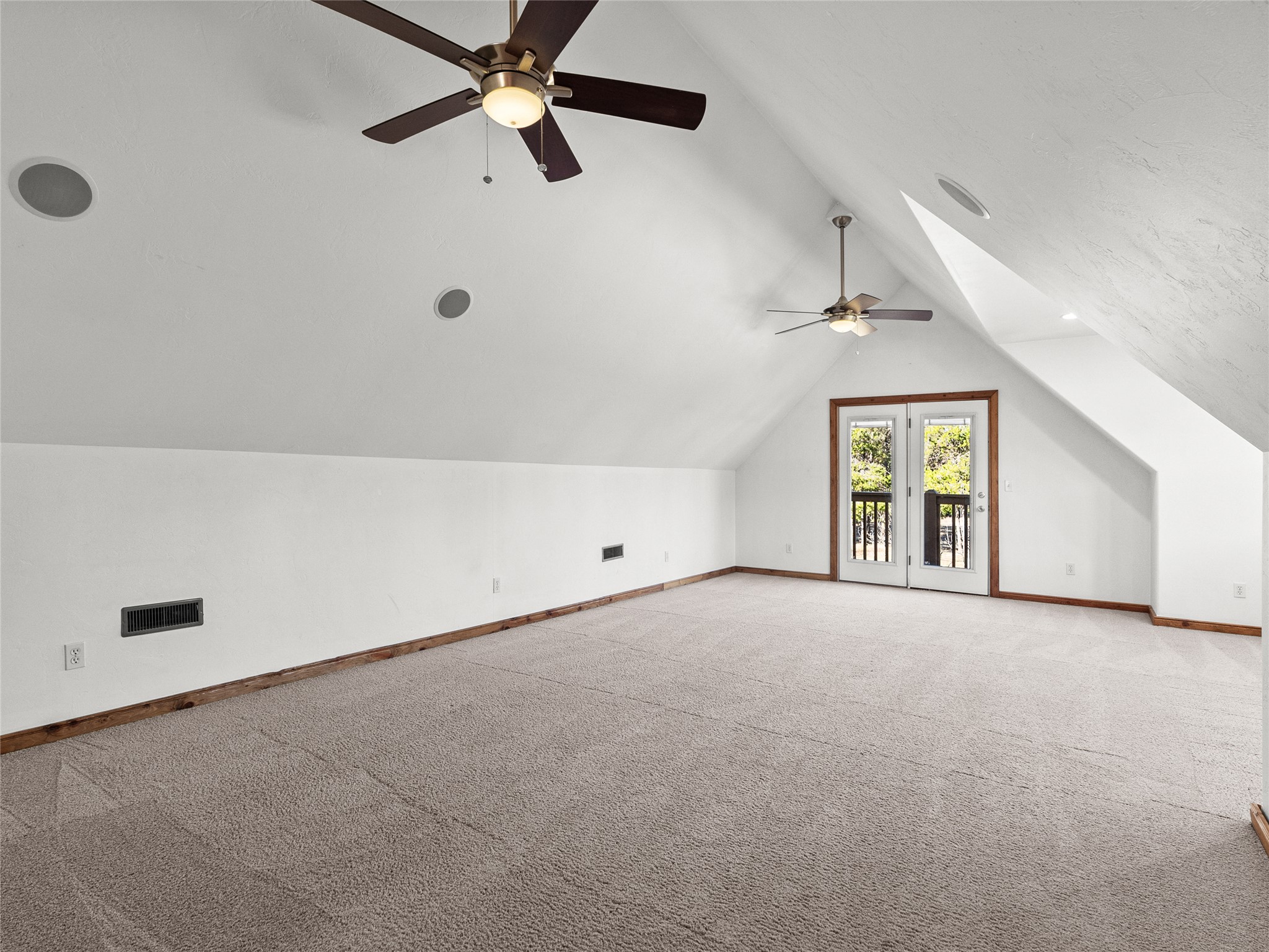 Carpeted vaulted room with two ceiling fans and double glass doors to a balcony.