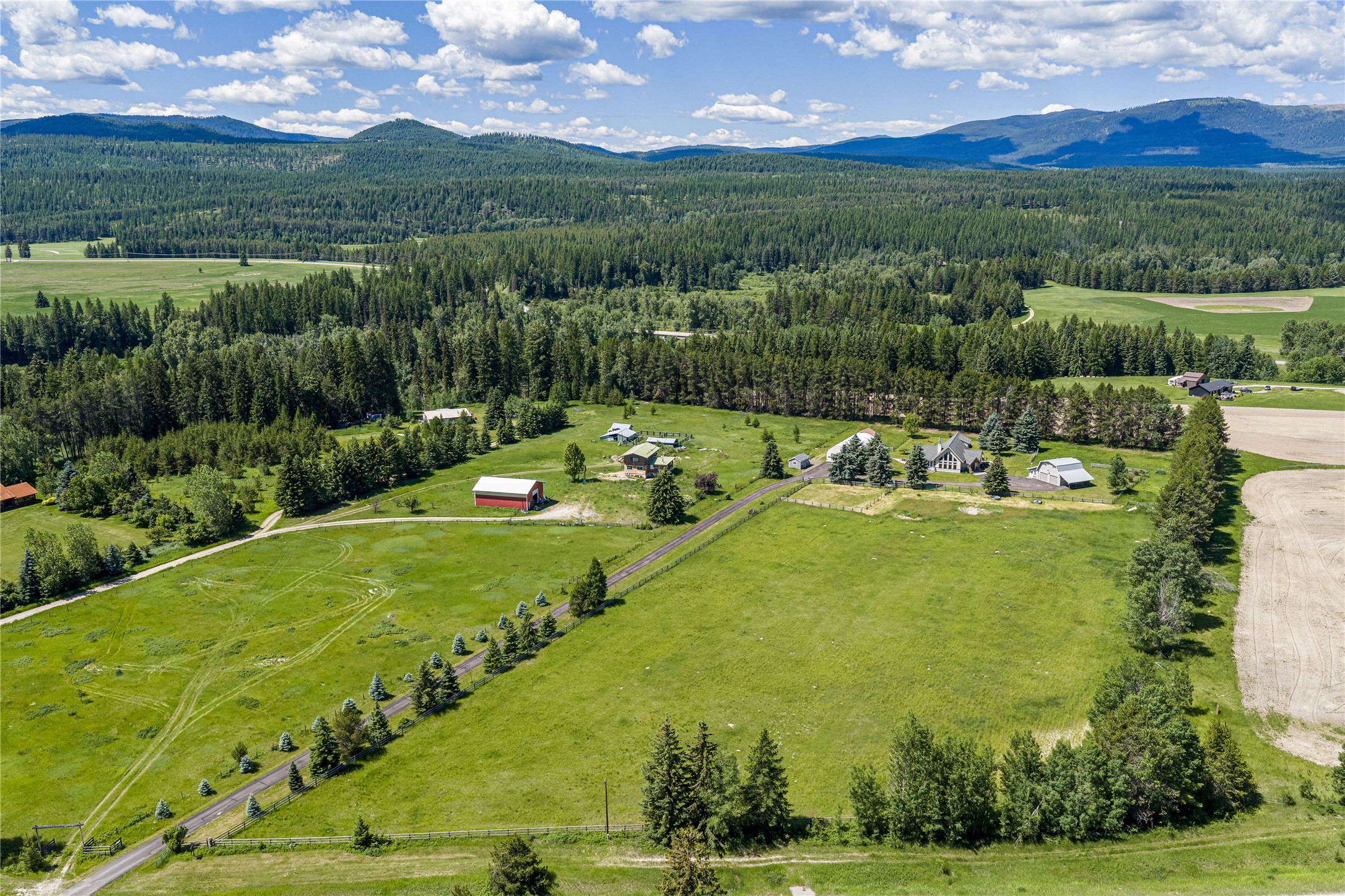 Aerial view of a rural property with open pasture, several buildings, and forested mountain views.