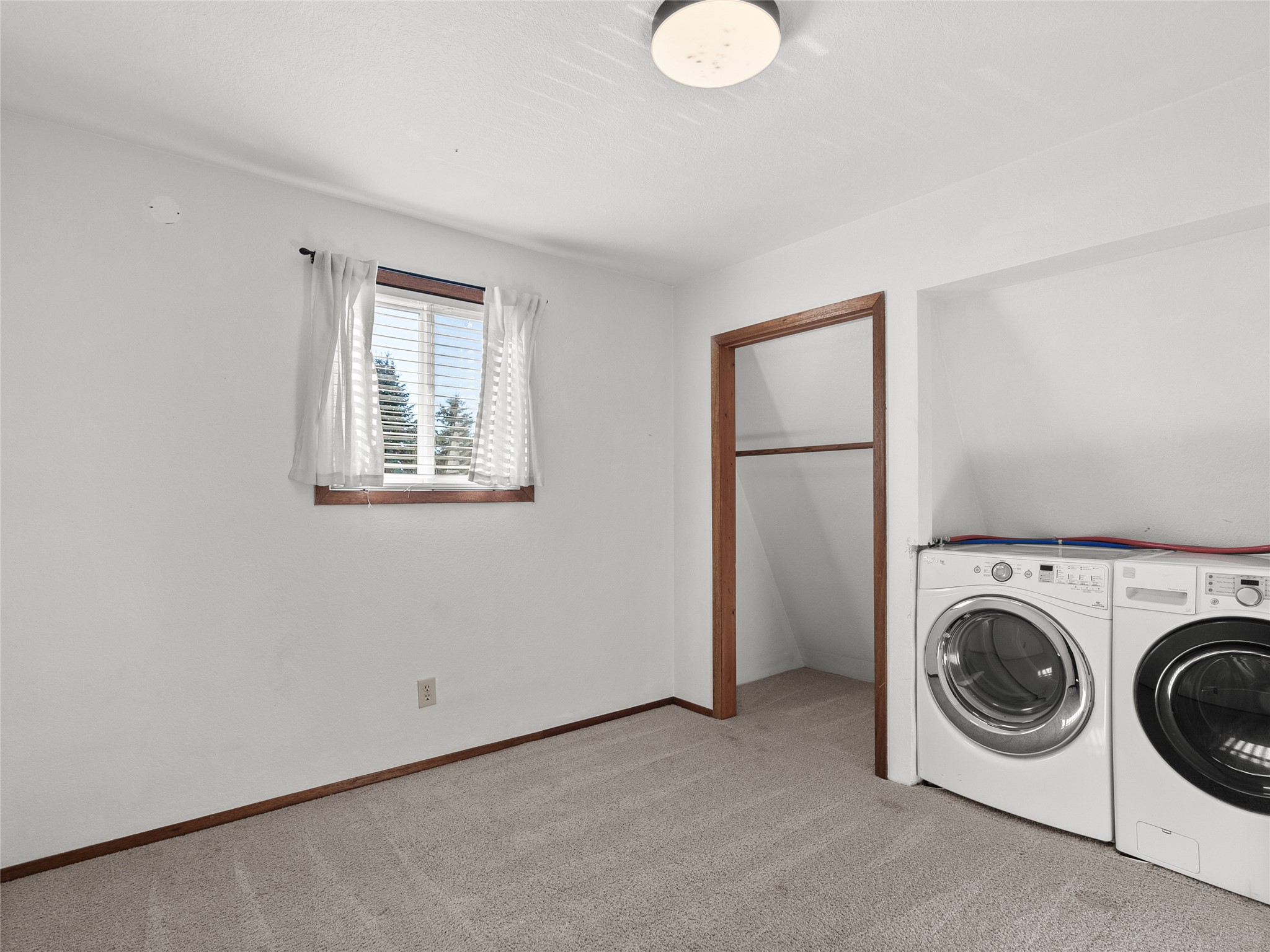 Laundry room with front-loading washer and dryer beside an open storage alcove.