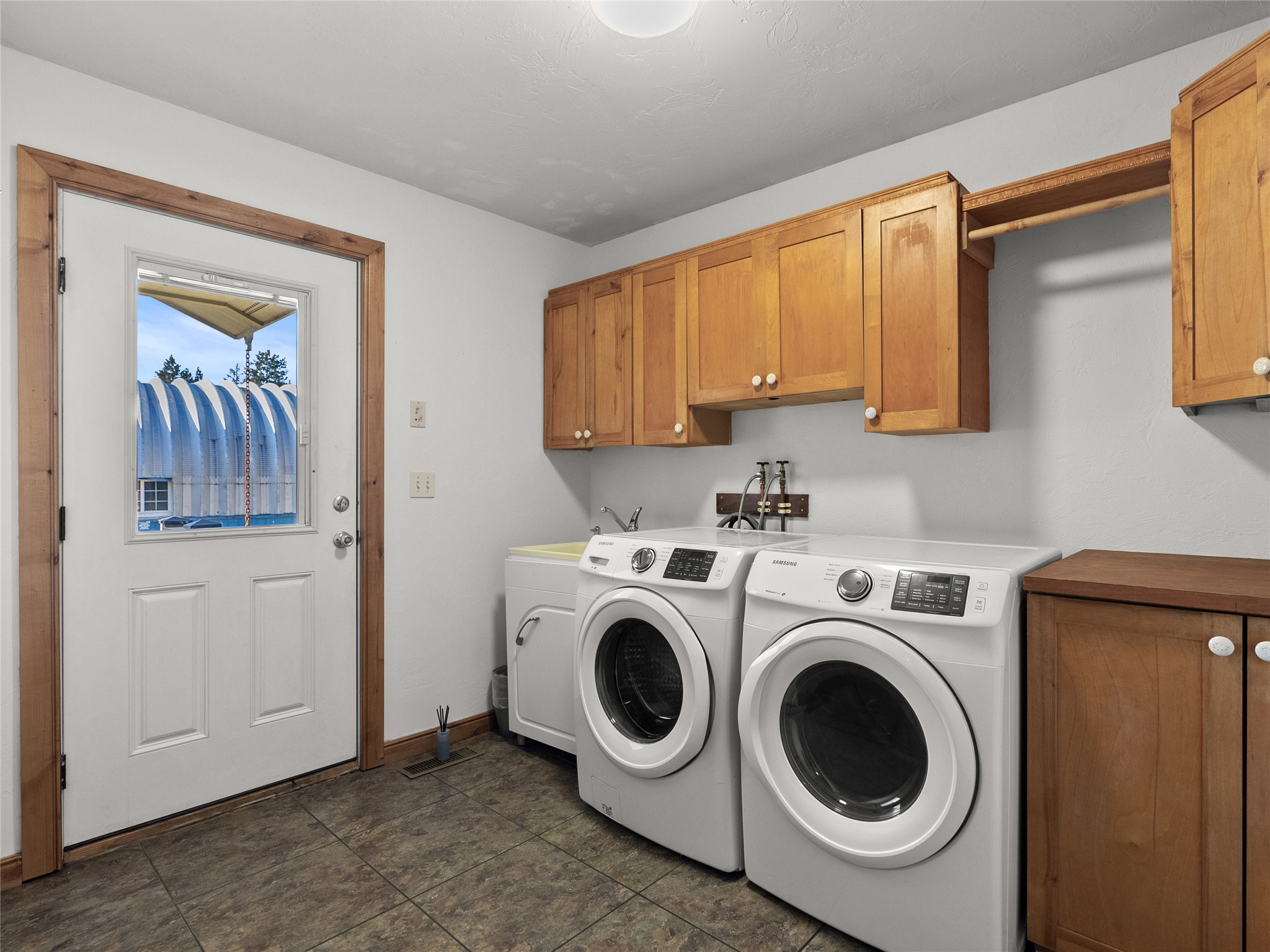 Laundry room with front-loading washer and dryer beneath wooden cabinets, beside a windowed exterior door.