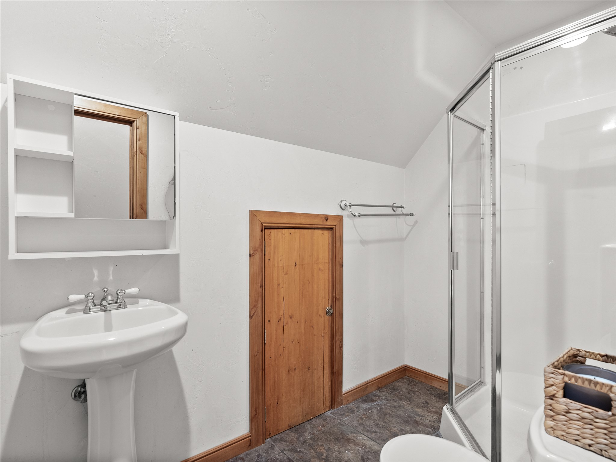 Bathroom with a glass shower, pedestal sink, and rustic wood door.