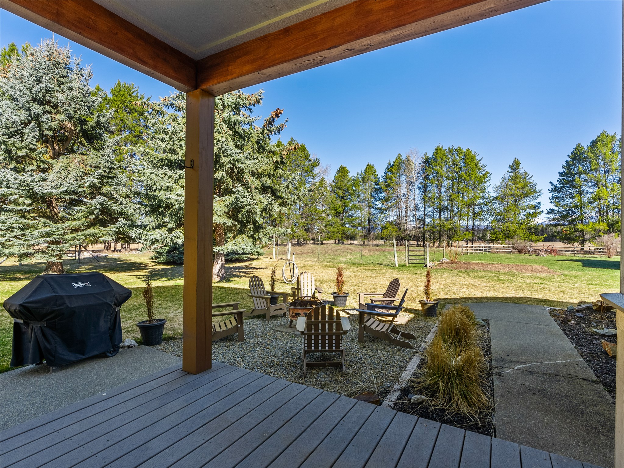 Covered deck overlooking a tree-lined yard, with Adirondack chairs around a fire pit.