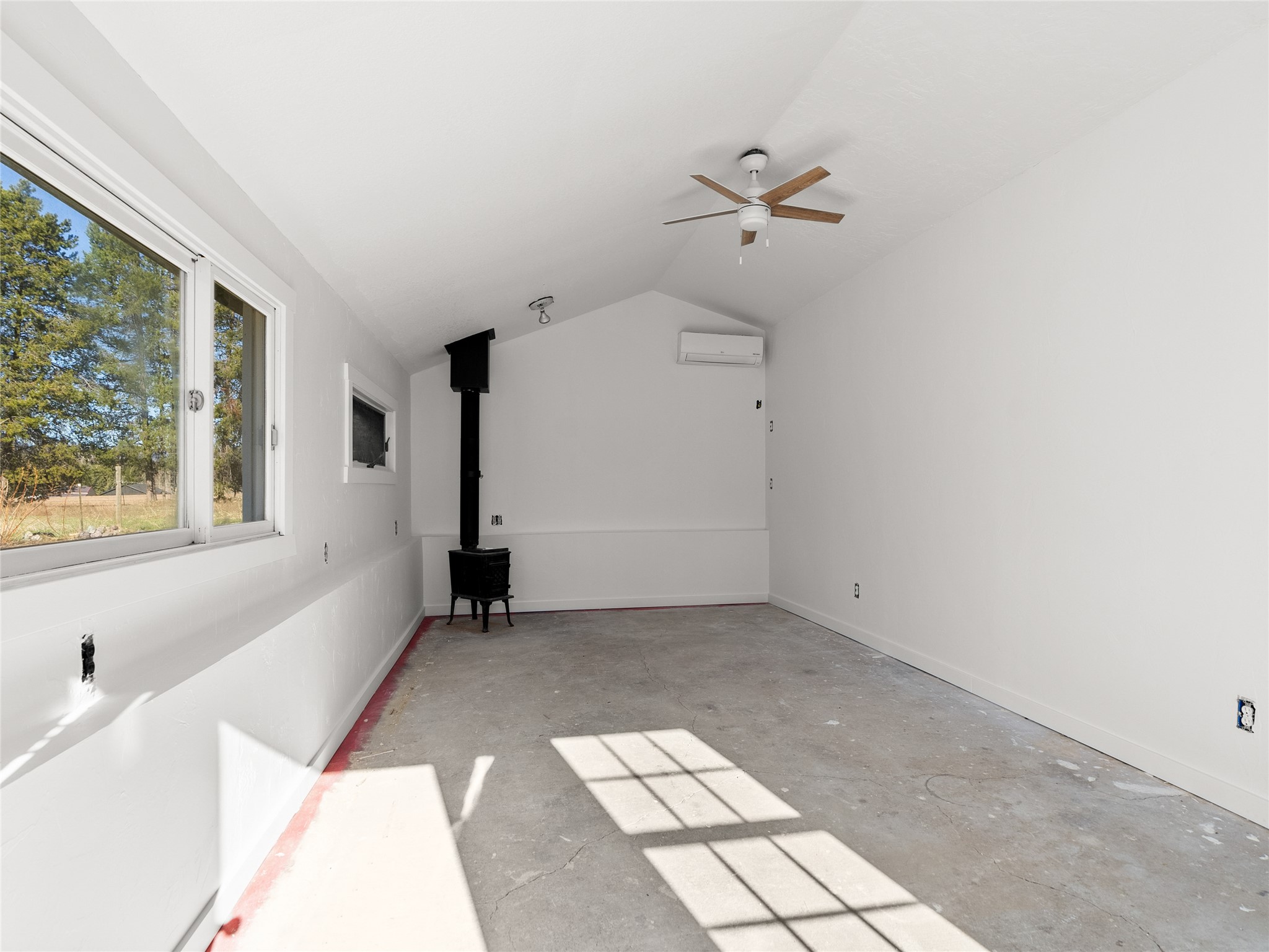 Vacant room with a concrete floor, large windows, and a black wood stove.