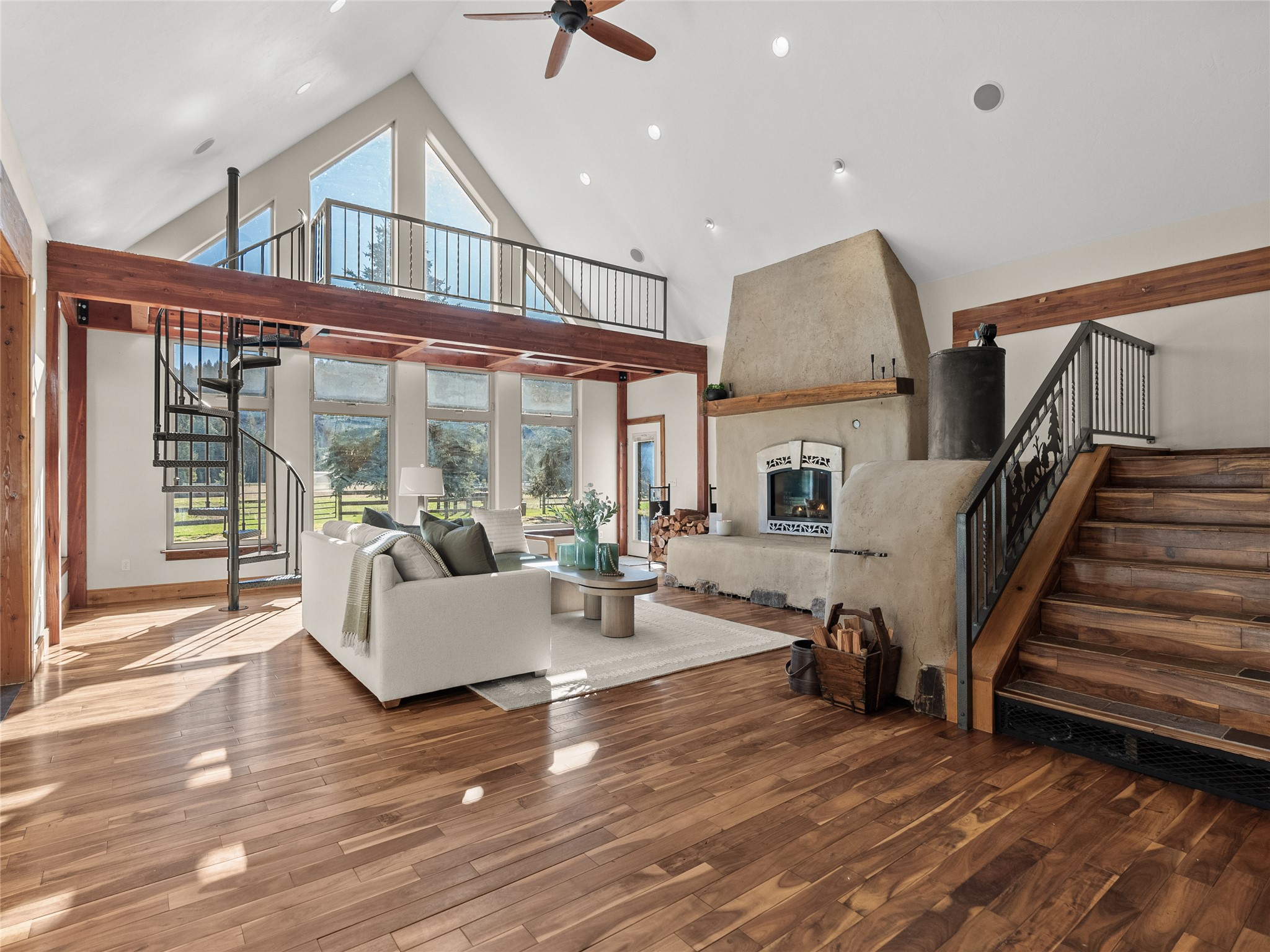 Living room with vaulted ceiling, timber mezzanine, spiral staircase, and stone fireplace.