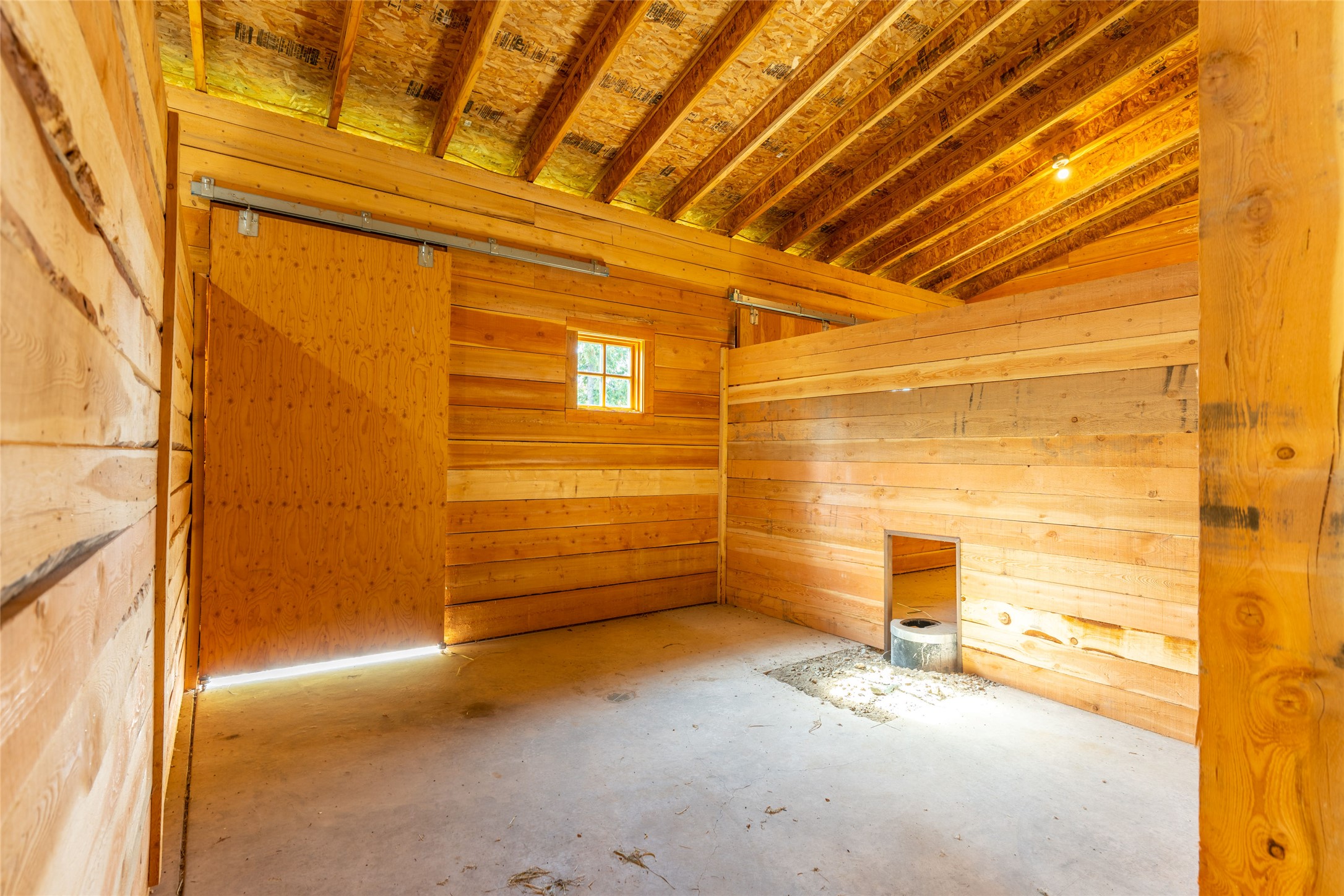 Rustic wooden barn interior with exposed roof beams, concrete floor, and sliding door.
